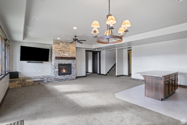 unfurnished living room with ceiling fan with notable chandelier, light colored carpet, a raised ceiling, and a fireplace