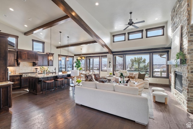 living room featuring a fireplace, dark hardwood / wood-style floors, beam ceiling, sink, and ceiling fan with notable chandelier