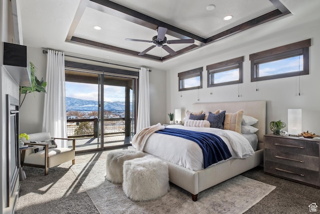 bedroom featuring ceiling fan, access to exterior, a tray ceiling, a mountain view, and dark carpet