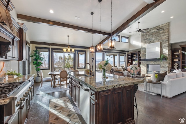 kitchen with a center island with sink, decorative light fixtures, a fireplace, ceiling fan with notable chandelier, and sink