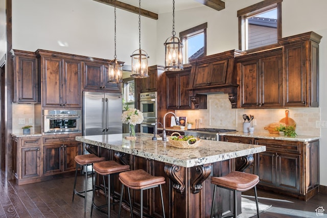 kitchen with decorative light fixtures, appliances with stainless steel finishes, an island with sink, and a high ceiling