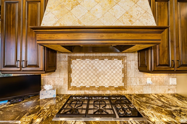 kitchen featuring premium range hood, stainless steel gas cooktop, tasteful backsplash, and dark stone counters