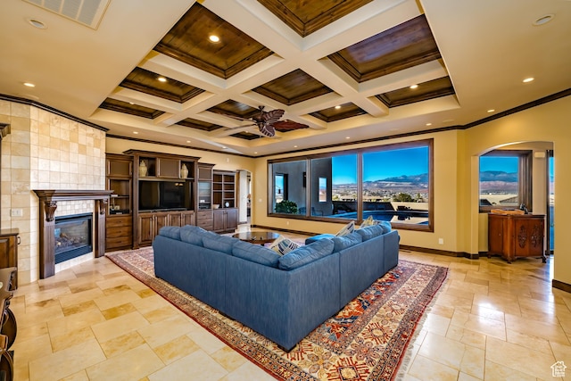 living room featuring ceiling fan, a tile fireplace, beamed ceiling, coffered ceiling, and ornamental molding