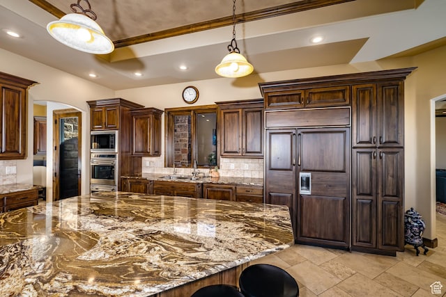 kitchen with a kitchen bar, a raised ceiling, tasteful backsplash, and dark stone countertops