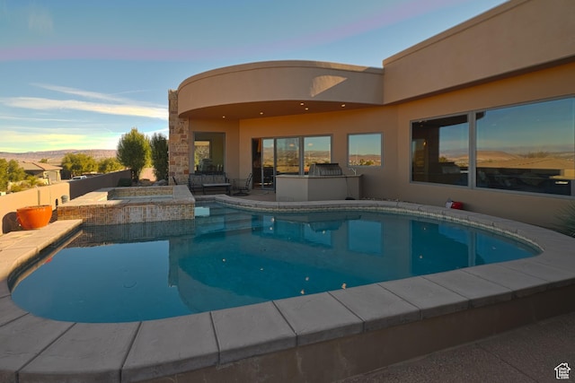 pool at dusk with an in ground hot tub and a patio area