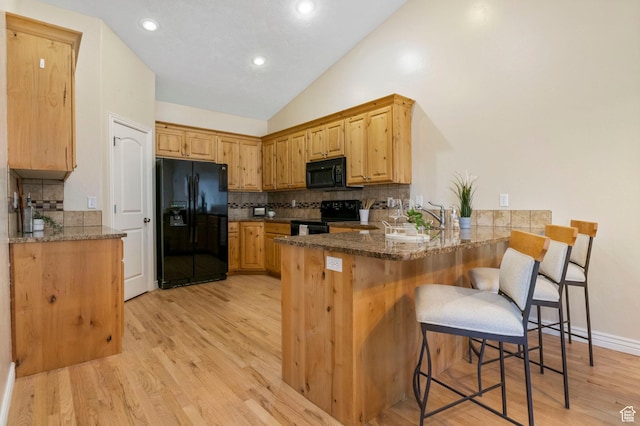 kitchen featuring black appliances, decorative backsplash, light hardwood / wood-style floors, kitchen peninsula, and a breakfast bar area
