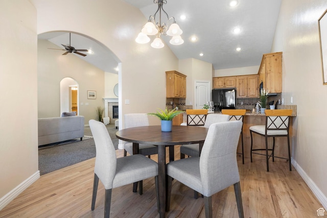 dining space with high vaulted ceiling, ceiling fan with notable chandelier, and light hardwood / wood-style flooring