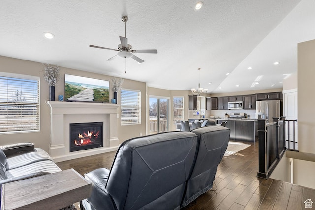 living room featuring recessed lighting, a glass covered fireplace, dark wood-style floors, and ceiling fan with notable chandelier