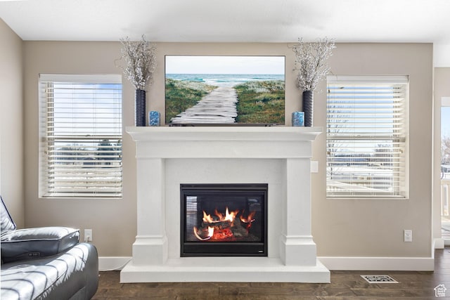 living area with a glass covered fireplace, a wealth of natural light, dark wood-style flooring, and visible vents