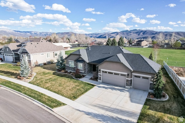 single story home with concrete driveway, stone siding, fence, a mountain view, and a garage