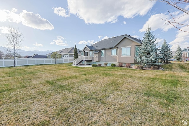rear view of house with fence, a lawn, and stucco siding