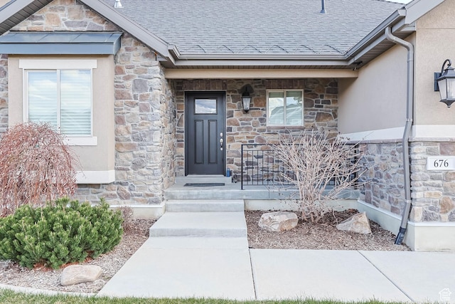 view of exterior entry featuring covered porch, stone siding, stucco siding, and a shingled roof