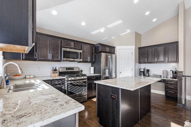 kitchen featuring a center island, a sink, vaulted ceiling, decorative backsplash, and appliances with stainless steel finishes