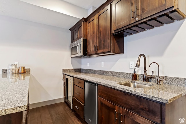 kitchen with stainless steel microwave, light stone counters, dark wood-style floors, dark brown cabinets, and a sink