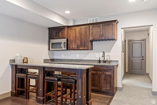 bar featuring visible vents, baseboards, a sink, wet bar, and stainless steel microwave