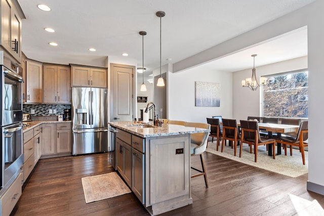 kitchen with recessed lighting, dark wood-style floors, light stone countertops, stainless steel appliances, and a sink