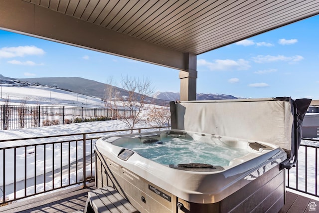 snow covered deck featuring fence, a mountain view, and a hot tub