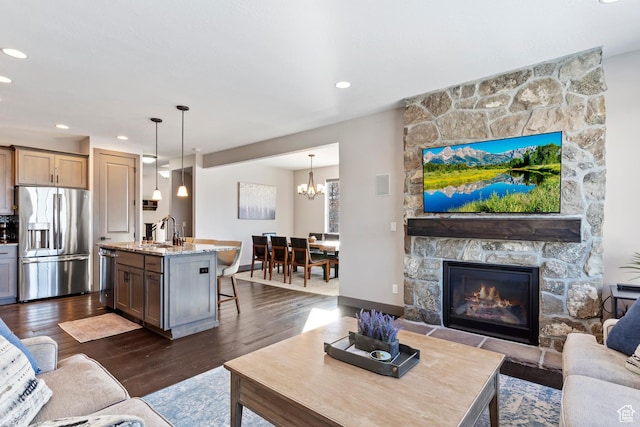 living area featuring recessed lighting, dark wood-type flooring, a stone fireplace, and an inviting chandelier