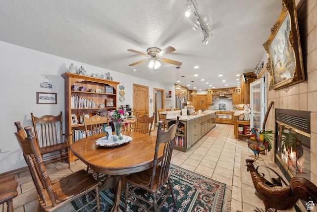 dining space with light tile patterned floors, rail lighting, ceiling fan, a textured ceiling, and a tiled fireplace