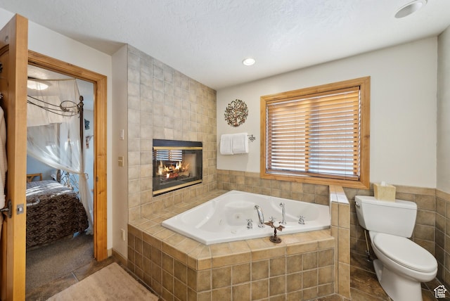 bathroom with a tile fireplace, tile walls, toilet, tiled tub, and a textured ceiling
