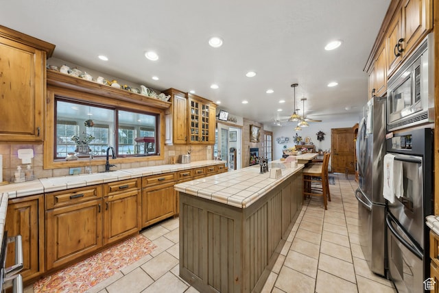 kitchen with a kitchen island, stainless steel microwave, hanging light fixtures, tile counters, and light tile patterned floors