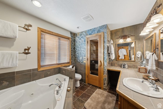 bathroom with tile walls, vanity, a textured ceiling, a tub, and toilet