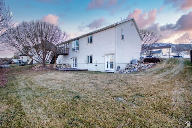 back house at dusk with a wooden deck, central AC, french doors, and a yard