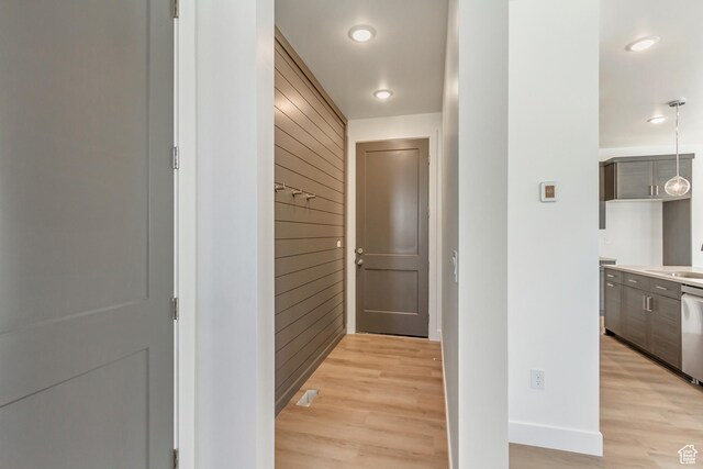 hallway with recessed lighting, wooden walls, a sink, light wood-style floors, and baseboards