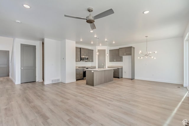 kitchen featuring an island with sink, stainless steel appliances, visible vents, open floor plan, and ceiling fan with notable chandelier