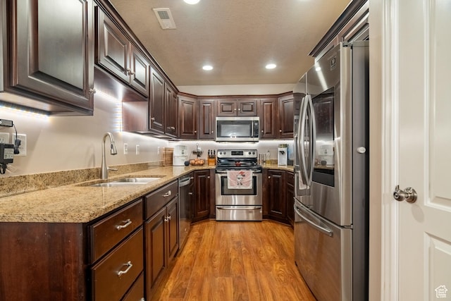 1841 E Whitetail Dr, Layton, UT 84040 - kitchen with appliances with stainless steel finishes, a sink, dark brown cabinets, light wood-type flooring, and light stone counters