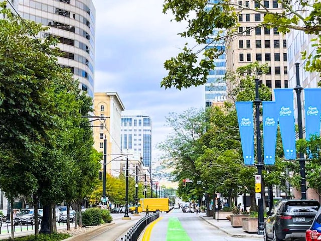 view of road featuring sidewalks, traffic lights, curbs, a city view, and street lights