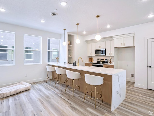 kitchen with a peninsula, appliances with stainless steel finishes, light wood-type flooring, and a breakfast bar area