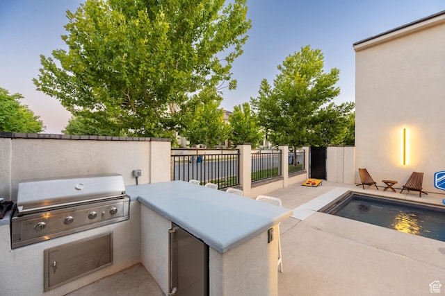 patio terrace at dusk featuring exterior kitchen and a grill