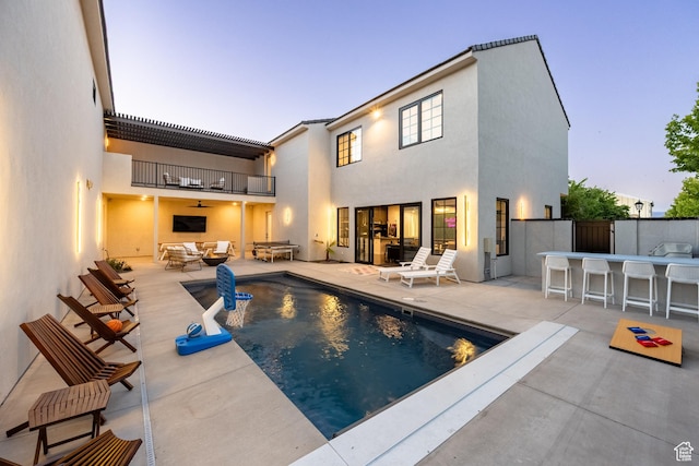 pool at dusk featuring ceiling fan, an outdoor hangout area, exterior bar, and a patio area