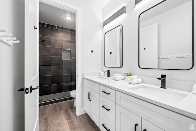 bathroom featuring toilet, vanity, wood-type flooring, and tiled shower