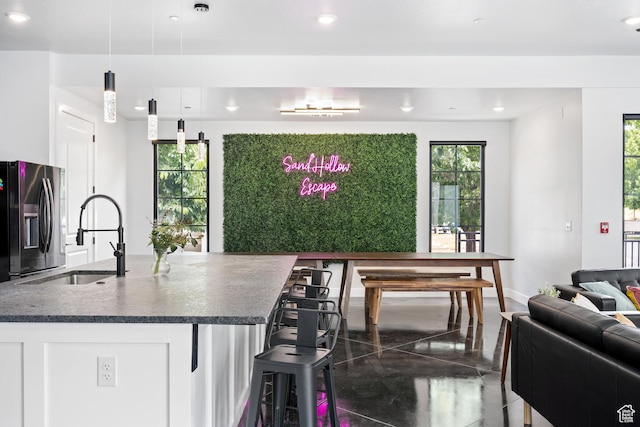 kitchen featuring a breakfast bar, stainless steel refrigerator with ice dispenser, sink, hanging light fixtures, and white cabinets