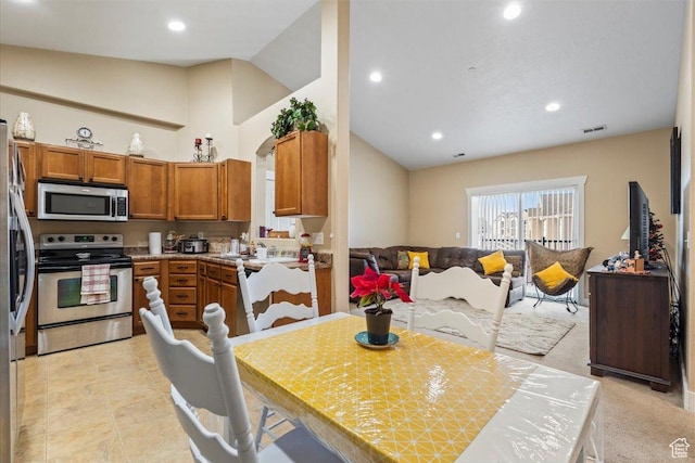 kitchen with appliances with stainless steel finishes, lofted ceiling, and light carpet