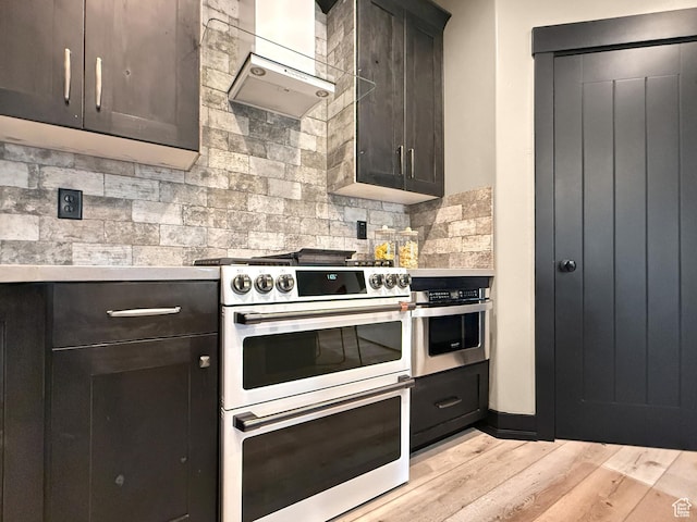 kitchen with stainless steel appliances, ventilation hood, decorative backsplash, light countertops, and light wood-type flooring