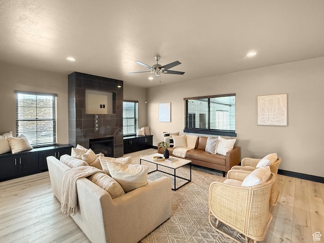 living area featuring plenty of natural light, light wood-style flooring, a ceiling fan, and a fireplace