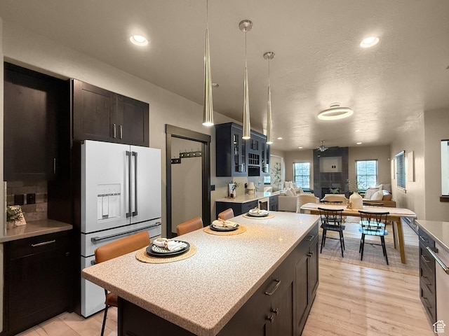 kitchen featuring high end white refrigerator, light countertops, open floor plan, hanging light fixtures, and a kitchen island