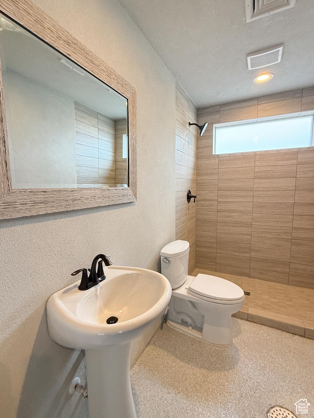 full bathroom with toilet, a textured wall, tiled shower, and visible vents