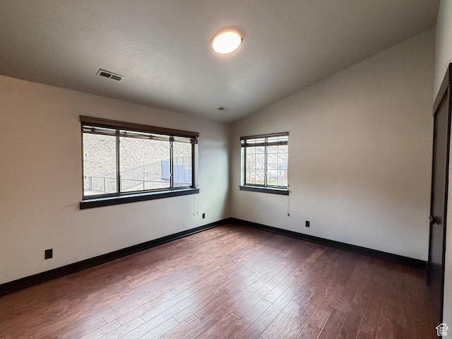 spare room featuring lofted ceiling, baseboards, dark wood-type flooring, and visible vents