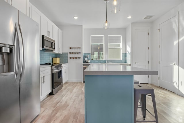 kitchen featuring decorative light fixtures, a breakfast bar area, stainless steel appliances, and white cabinetry