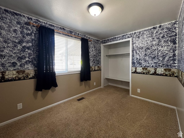 unfurnished bedroom with carpet flooring, a textured ceiling, visible vents, baseboards, and wallpapered walls