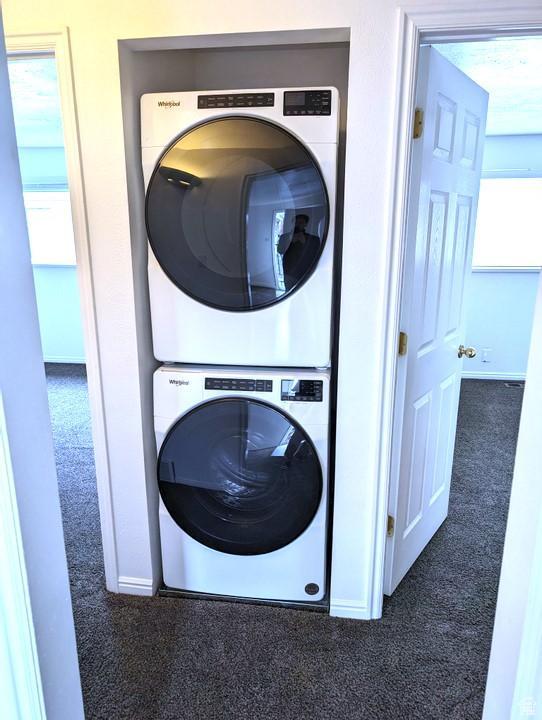laundry area with stacked washer and clothes dryer and dark carpet