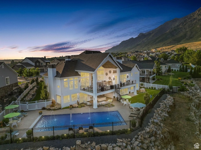 back house at dusk featuring a patio, pool water feature, a mountain view, a balcony, and a fenced in pool