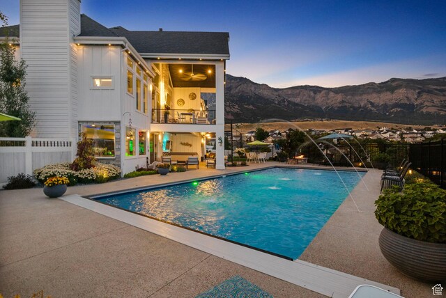pool at dusk with pool water feature, a mountain view, and a patio