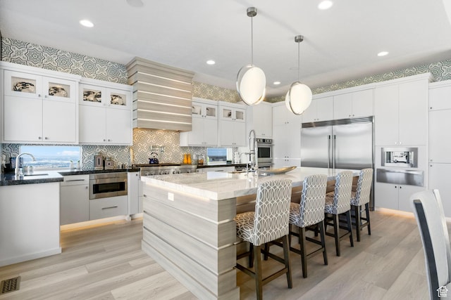kitchen featuring appliances with stainless steel finishes, white cabinetry, decorative light fixtures, and a kitchen island with sink