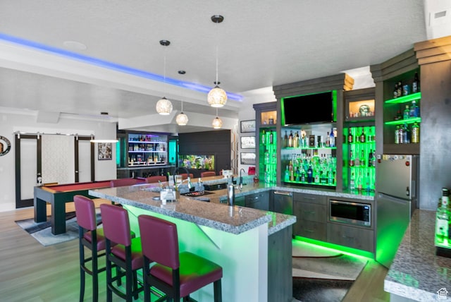 kitchen with decorative light fixtures, dark stone countertops, stainless steel refrigerator, light hardwood / wood-style flooring, and a breakfast bar area