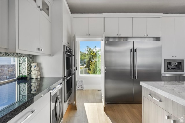 kitchen with white cabinets, dark stone counters, stainless steel appliances, and light hardwood / wood-style flooring
